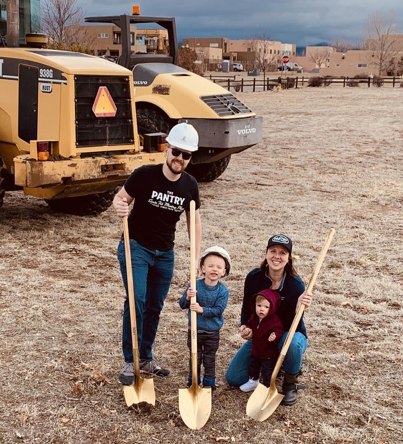 Michael, Lauren and their kids in hard hats with shovels, breaking ground on a dirt lot.